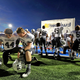 Two Permian players kneel on the side of the field before the start of a game.